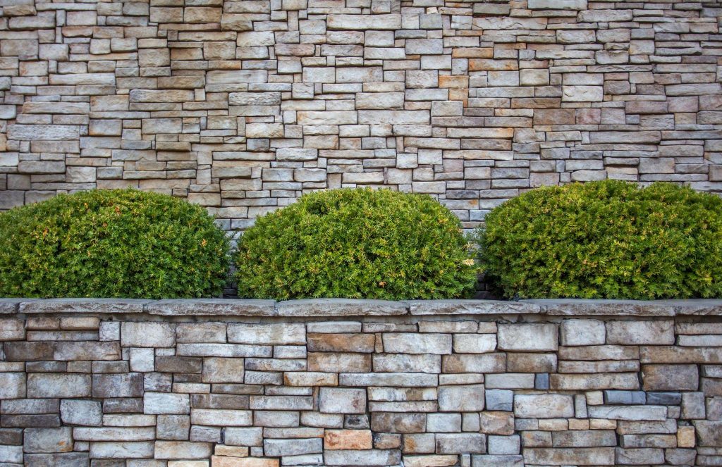 Rounded green shrubs in planter box against a gray and brown brick wall