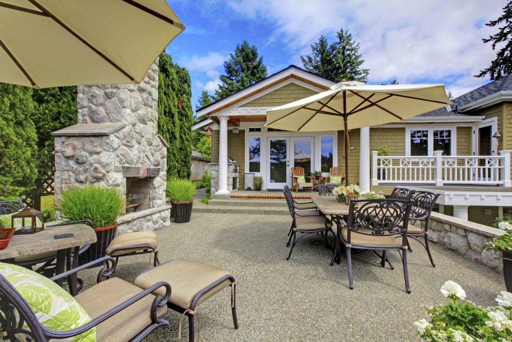 Patio area with stone fireplace and concrete floor. Patio table set with umbrella and deck chairs.