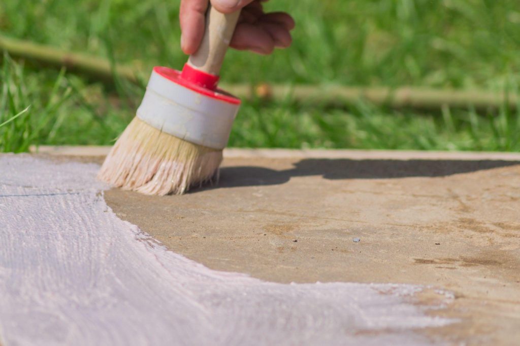 Workers hand holding a brush and puts primer on concrete floor