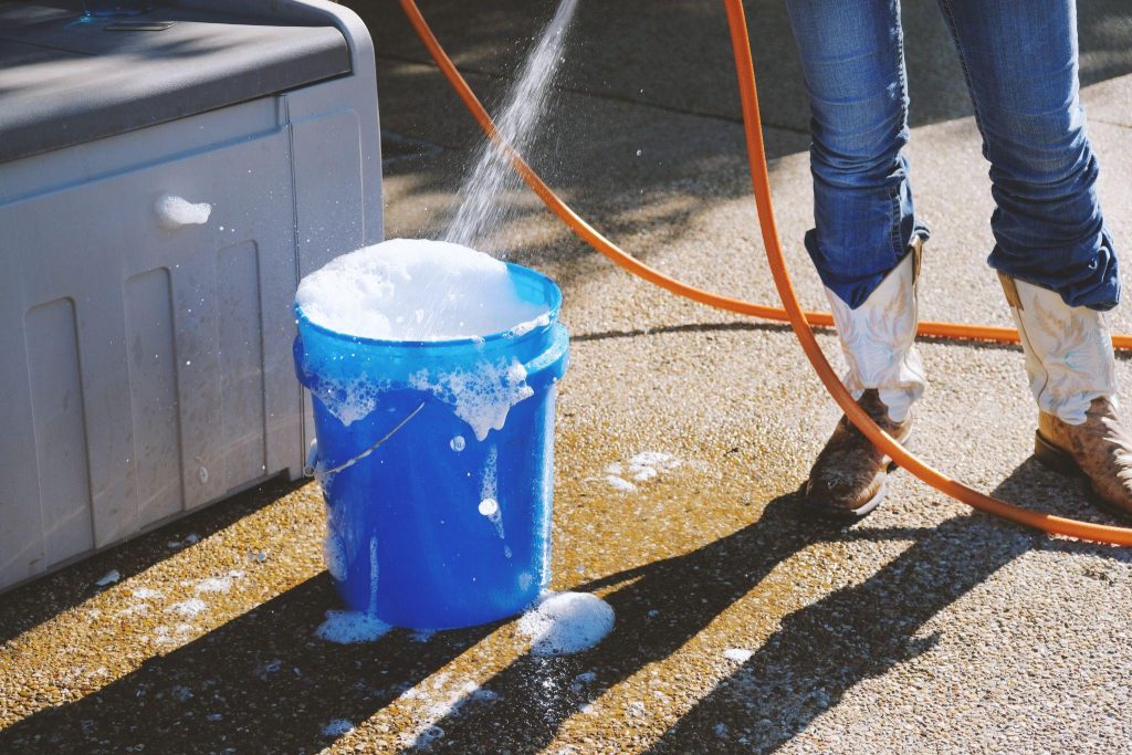 woman in cowboy boots filling blue bucket of soapy water to do cleaning chores.