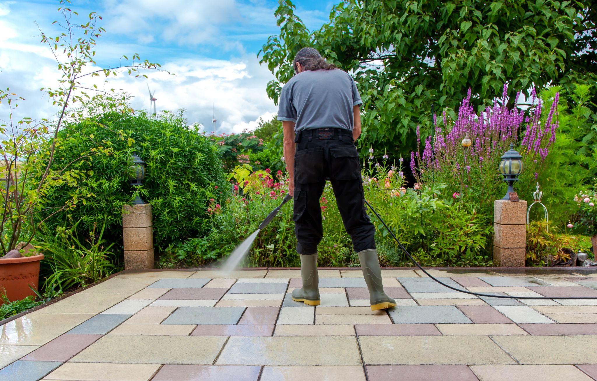 Cleaning stone slabs on patio with the high-pressure cleaner. Person worker in rubber boots cleaning the outdoors floor.