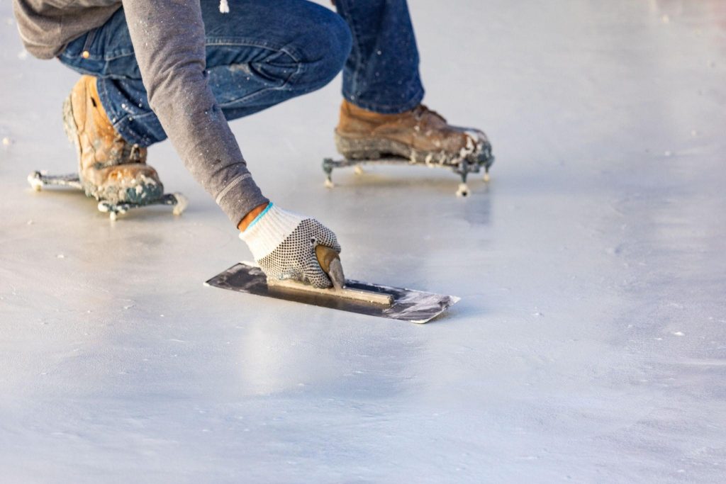 Worker wearing spiked shoes smoothing wet pool plaster with trowel