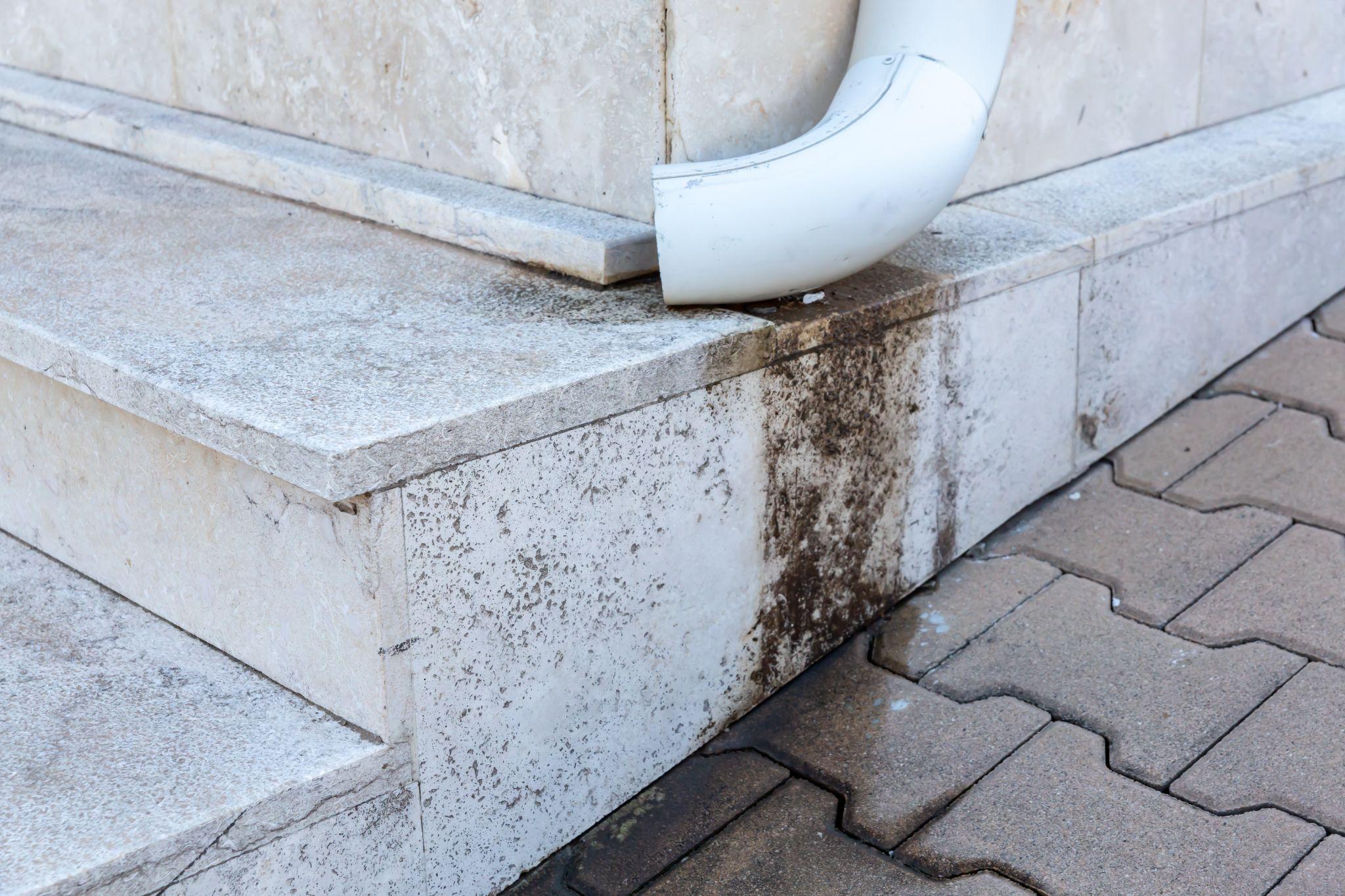 Downspout drainage issue on stone steps highlighting potential maintenance and water damage concerns.